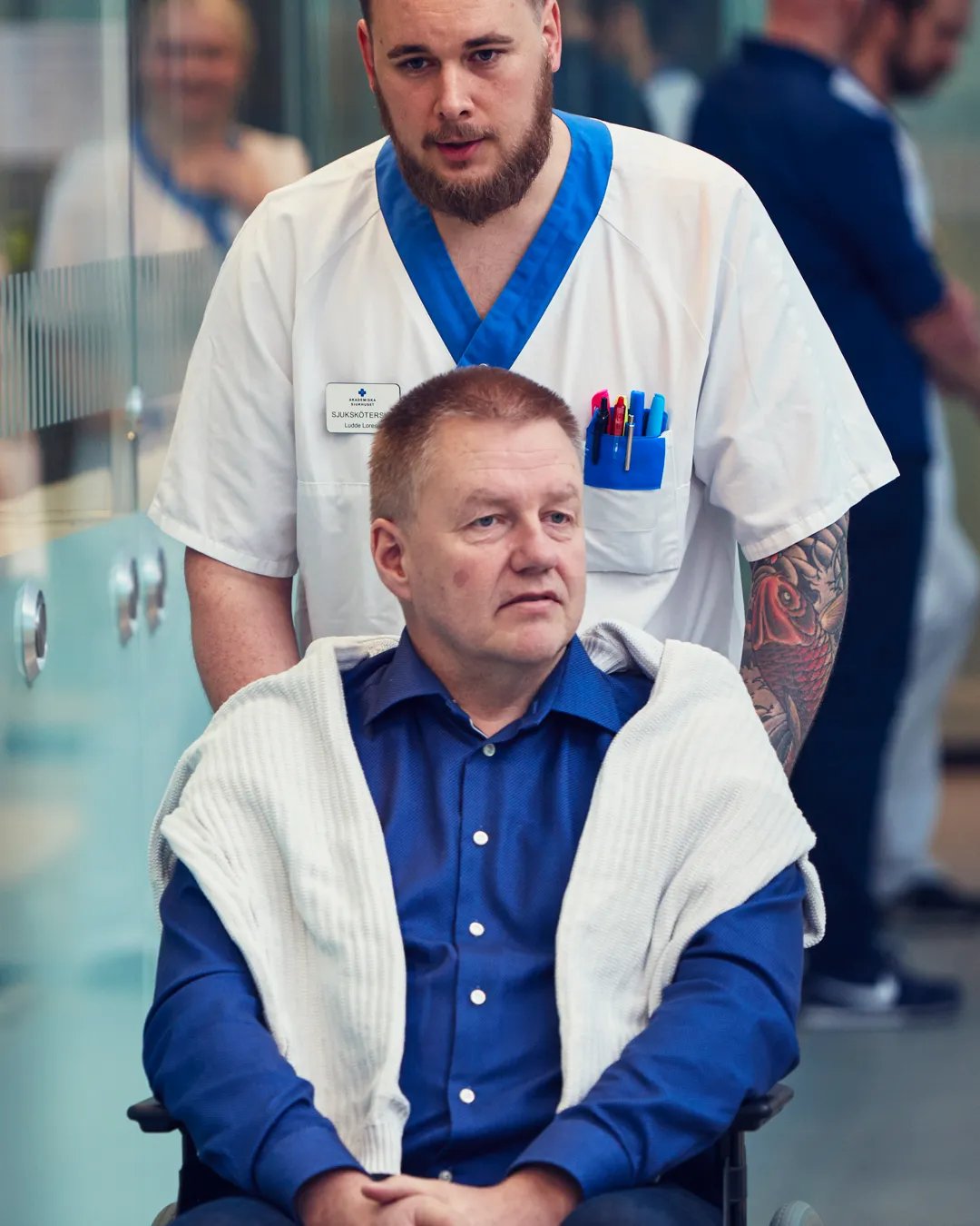 En man blir skjutsad i en rullstol av en sjuksköterska.